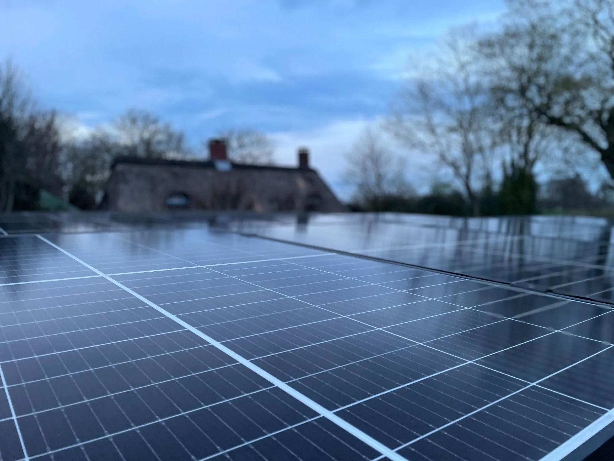 Weitwinkelaufnahme einer aufgeständerten Photovoltaikanlage auf einem Carport in der Dämmerung