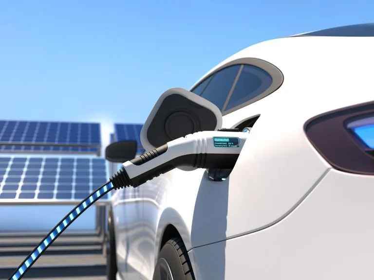 Ladekabel steckt in einem weißen Elektroauto, im Hintergrund Photovoltaikmodule